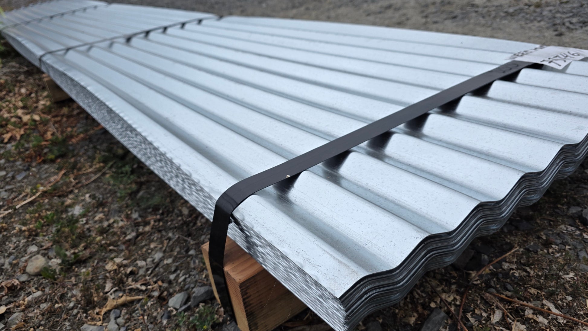 A bundle of heavy-duty 24-gauge galvanized corrugated steel roofing panels at Valley Outdoor Supply in Lake Stevens. These 25.5-inch wide legacy panels are shown stacked and strapped on wooden blocks, highlighting the thick, industrial-grade profile used for PNW shops and barns.