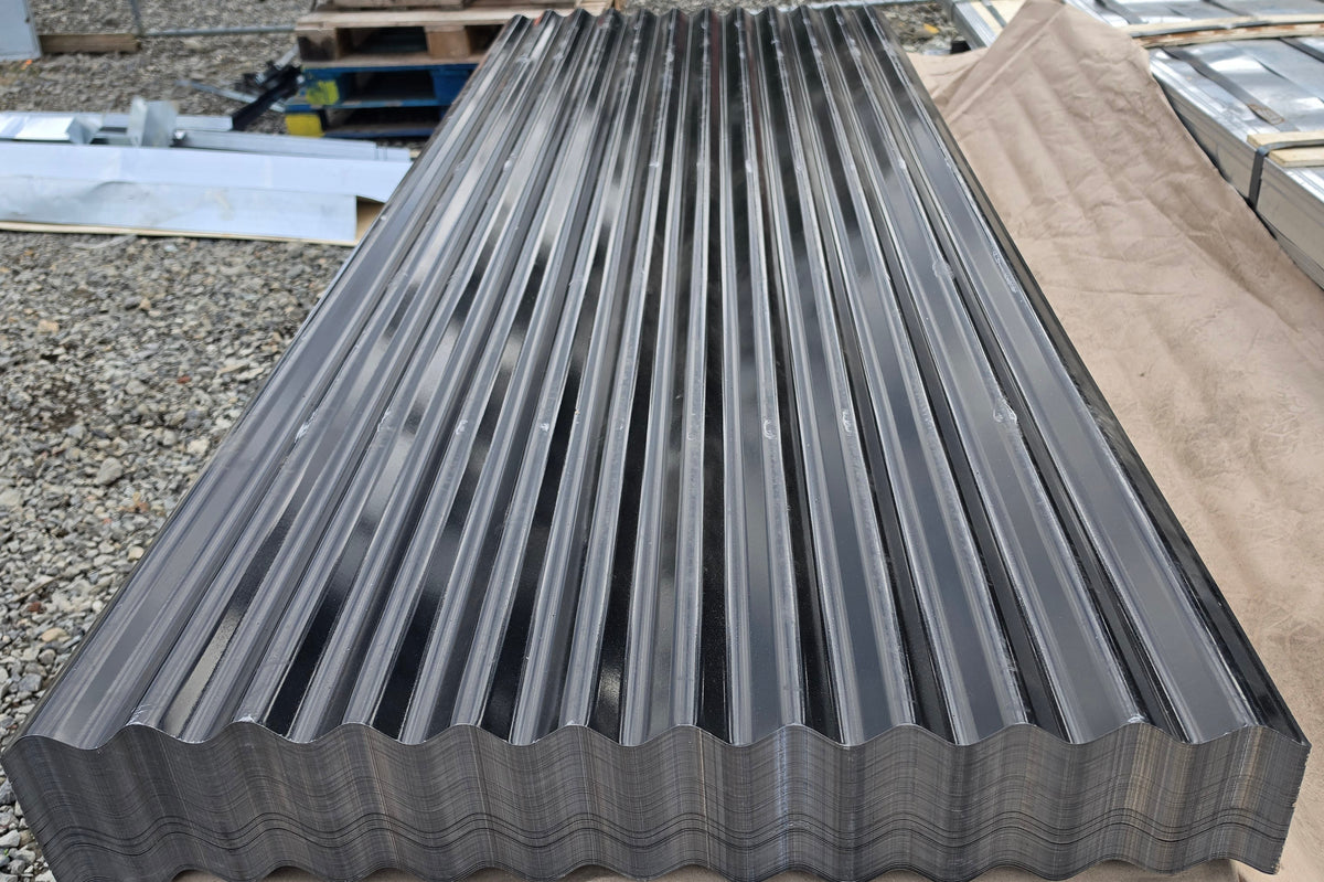 A stack of dark gray corrugated metal roofing panels resting on a tan protective sheet in an outdoor warehouse or yard setting.