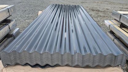 A stack of galvanized corrugated metal roofing panels resting on a tan sheet of paper on an outdoor gravel surface.