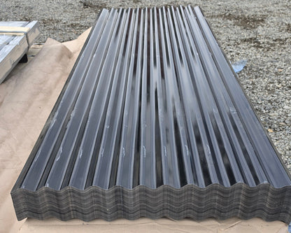 A long rectangular sheet of dark gray corrugated metal roofing material laid flat on a tan tarp in an outdoor industrial yard.