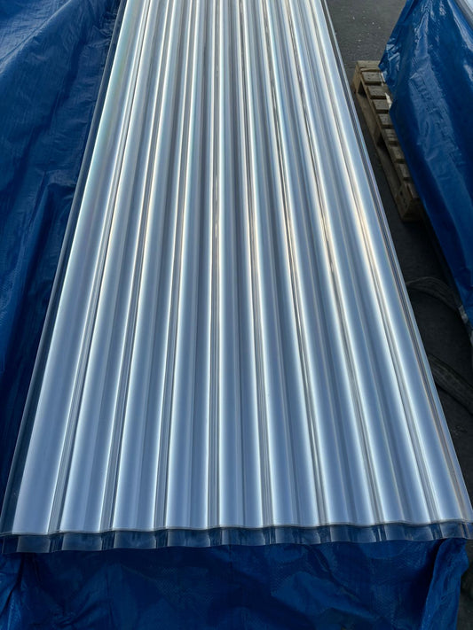 A stack of clear, corrugated polycarbonate roofing panels resting on a blue tarp at Valley Outdoor Supply. These heavy-duty 0.9mm panels are shown in their natural transparent state, highlighting the clean profile used for greenhouses and patio daylighting in the Pacific Northwest