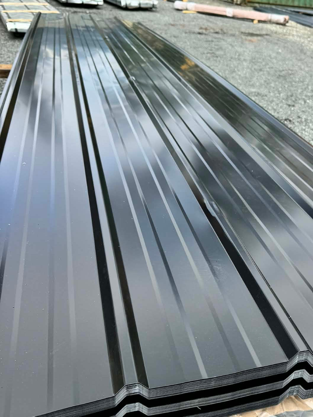 Metal roofing sheets on a construction site with a truck and containers in the background.